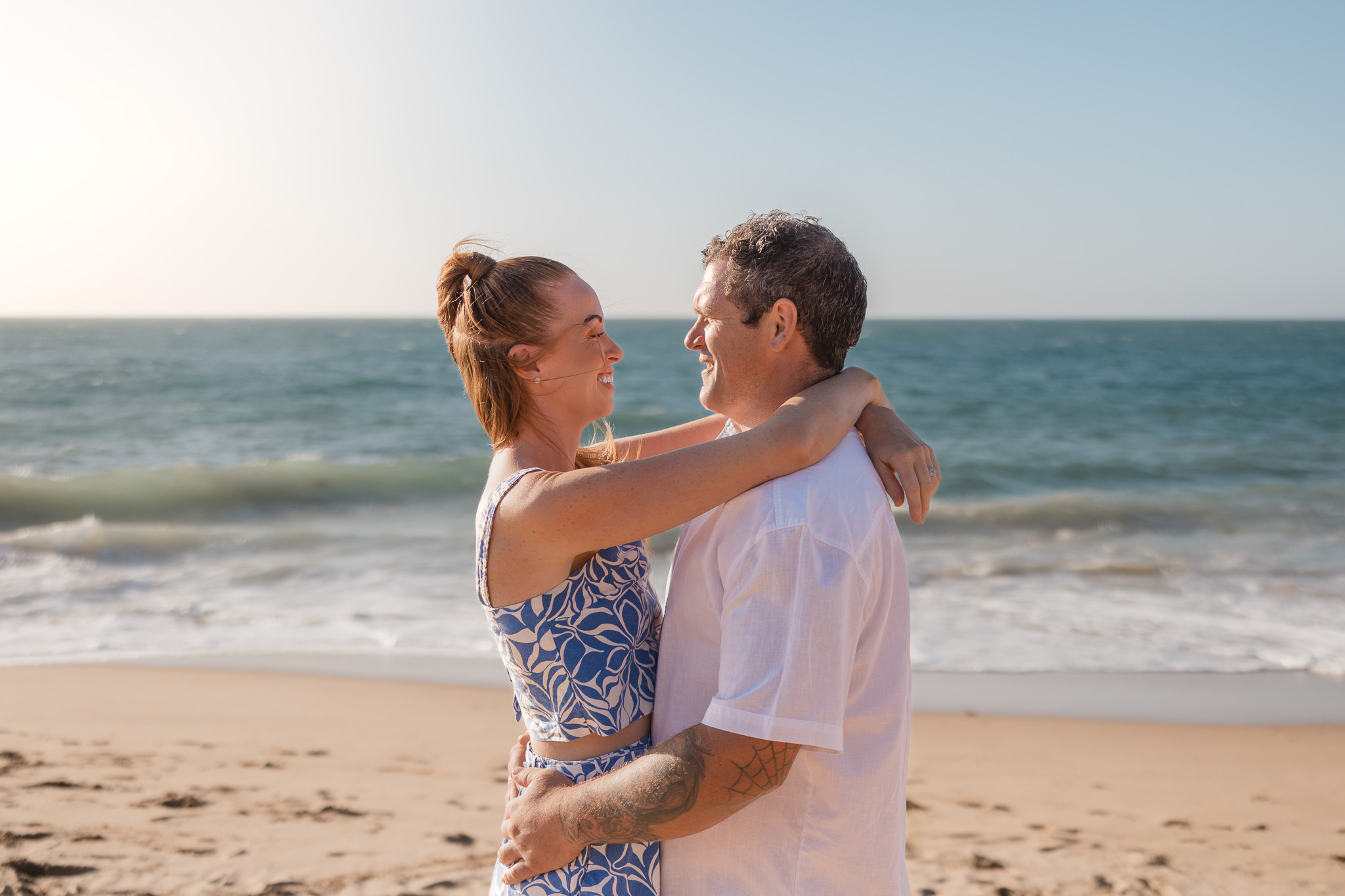 Smiling couple embracing on a sandy Perth beach with the ocean behind them