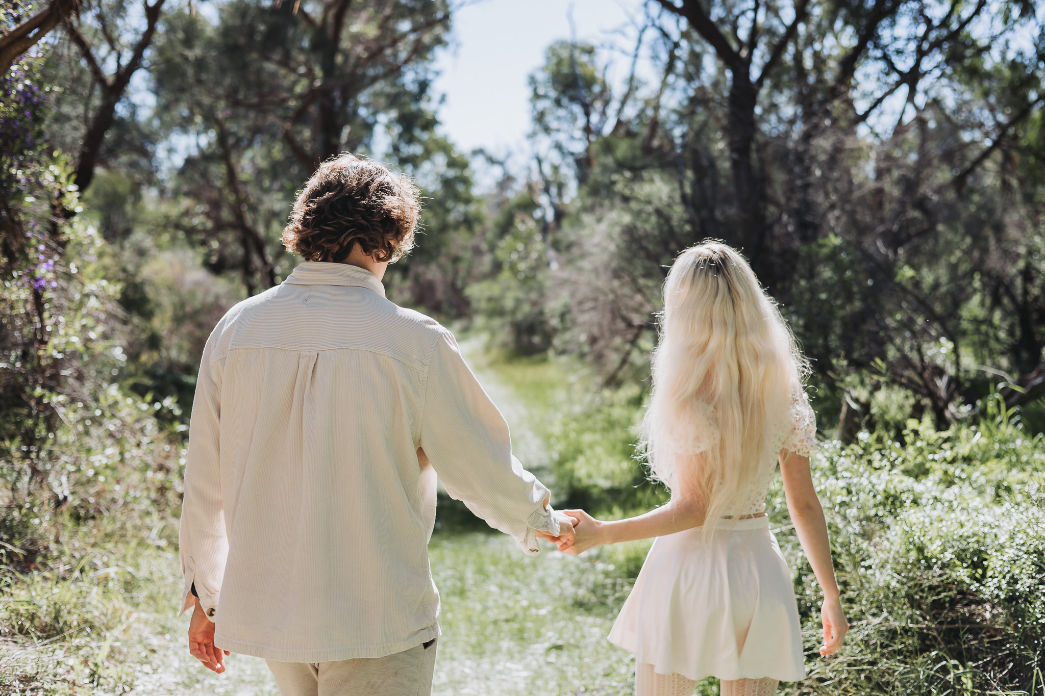 Couple walking away hand in hand along a bright wooded path near Perth