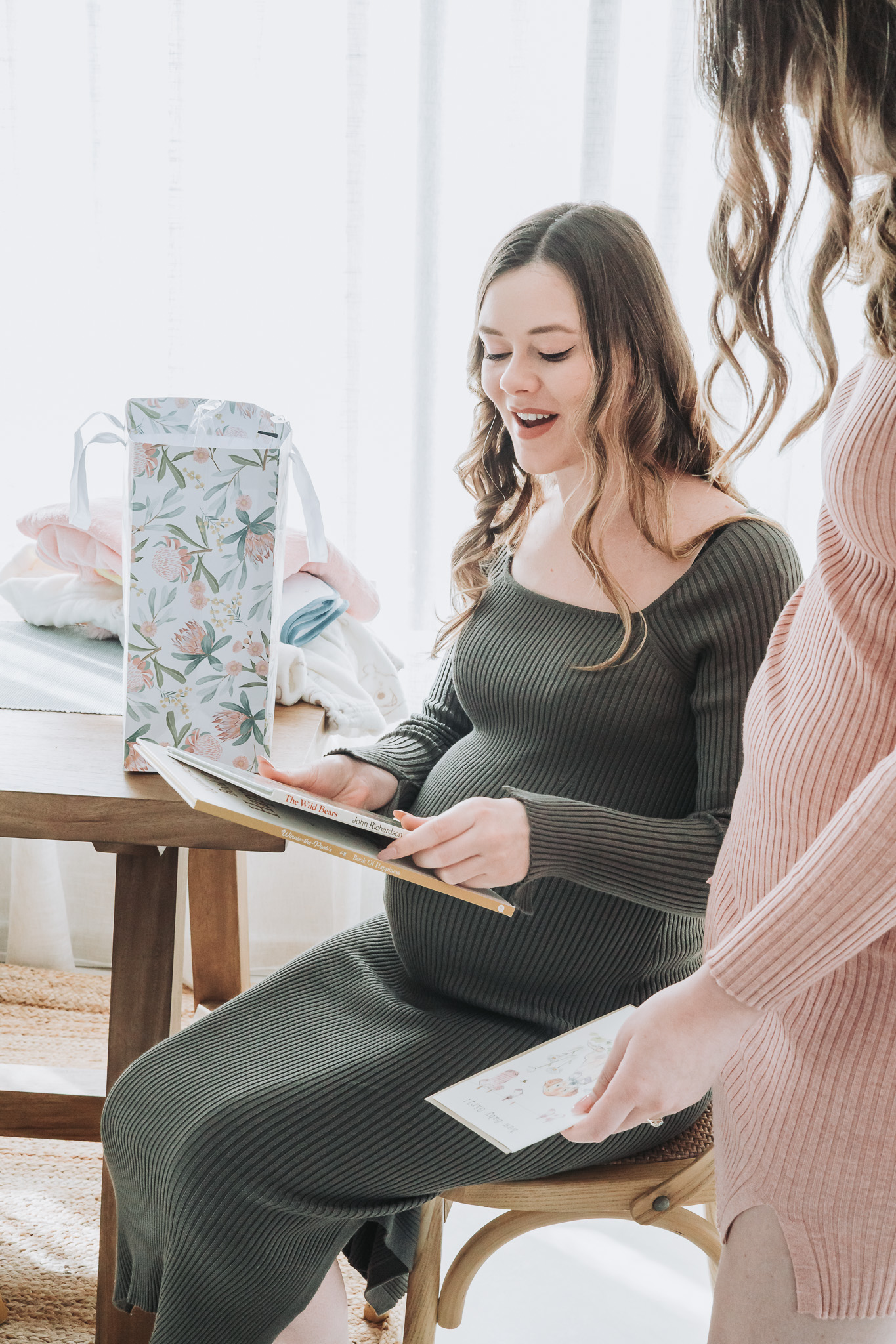 Expectant mother in an olive dress opening children's books at a bright Perth baby shower