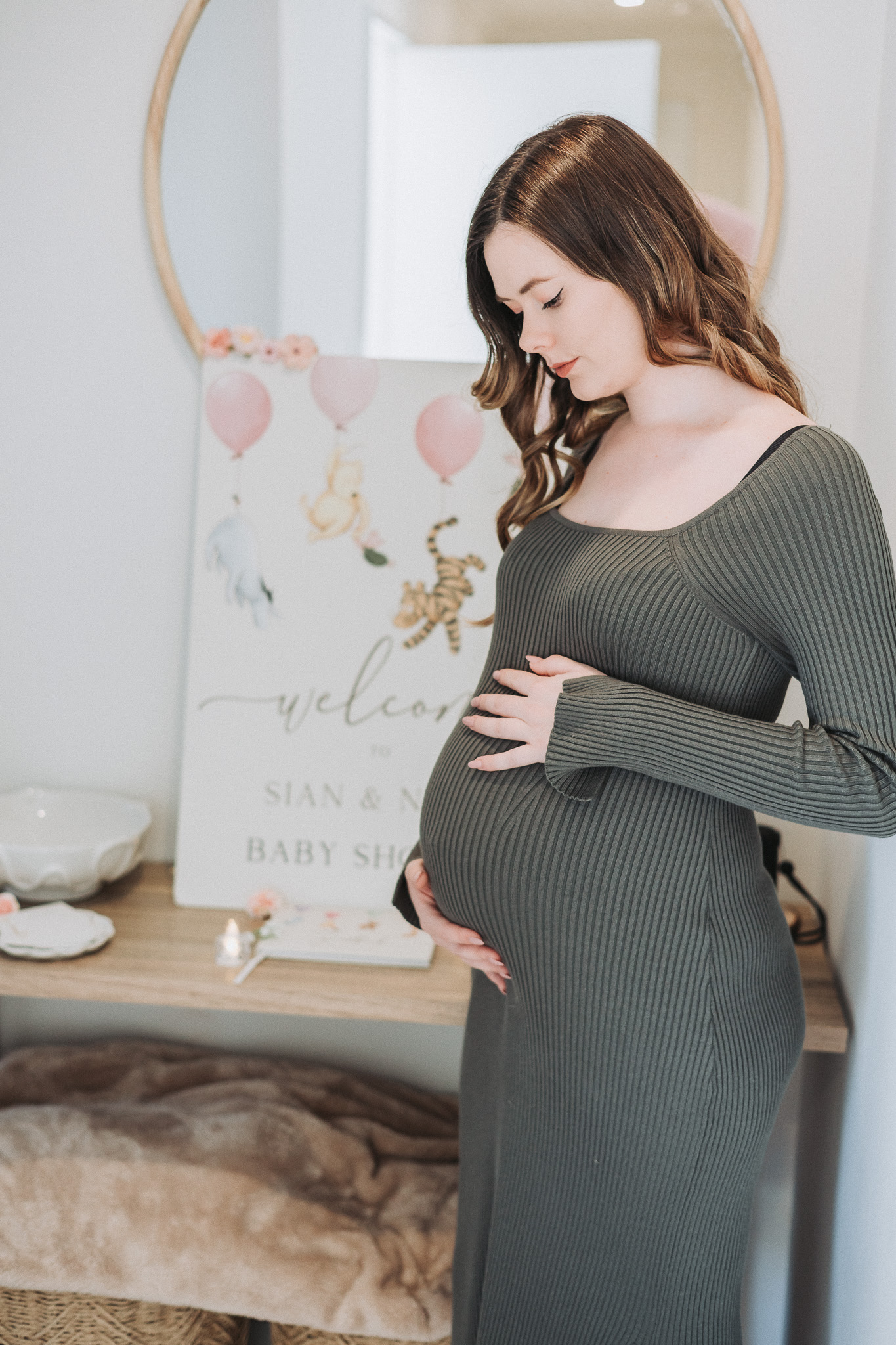 Expectant mother cradling her bump beside a Winnie the Pooh baby shower welcome sign