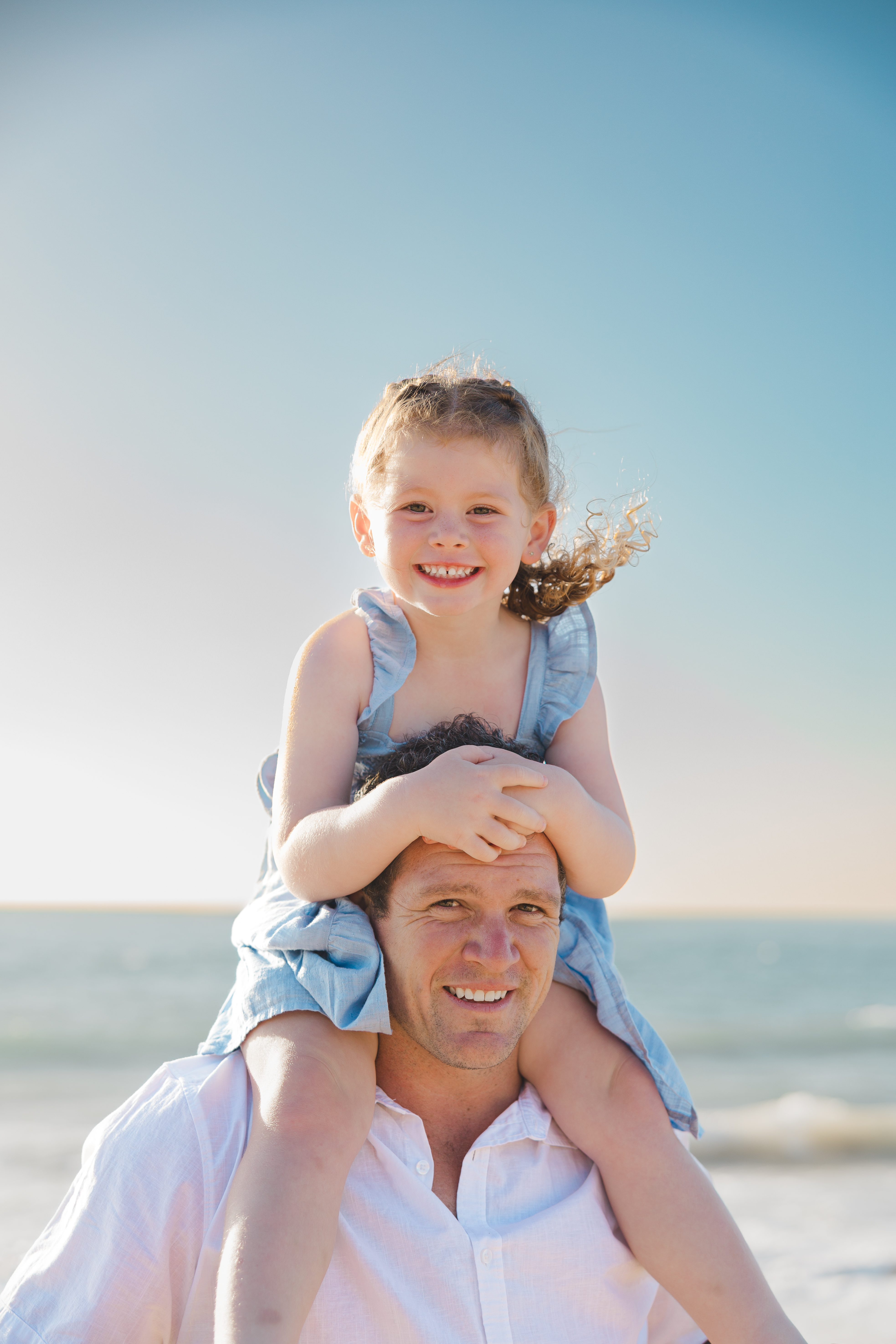 Father carrying his daughter on his shoulders and smiling on a bright Perth beach