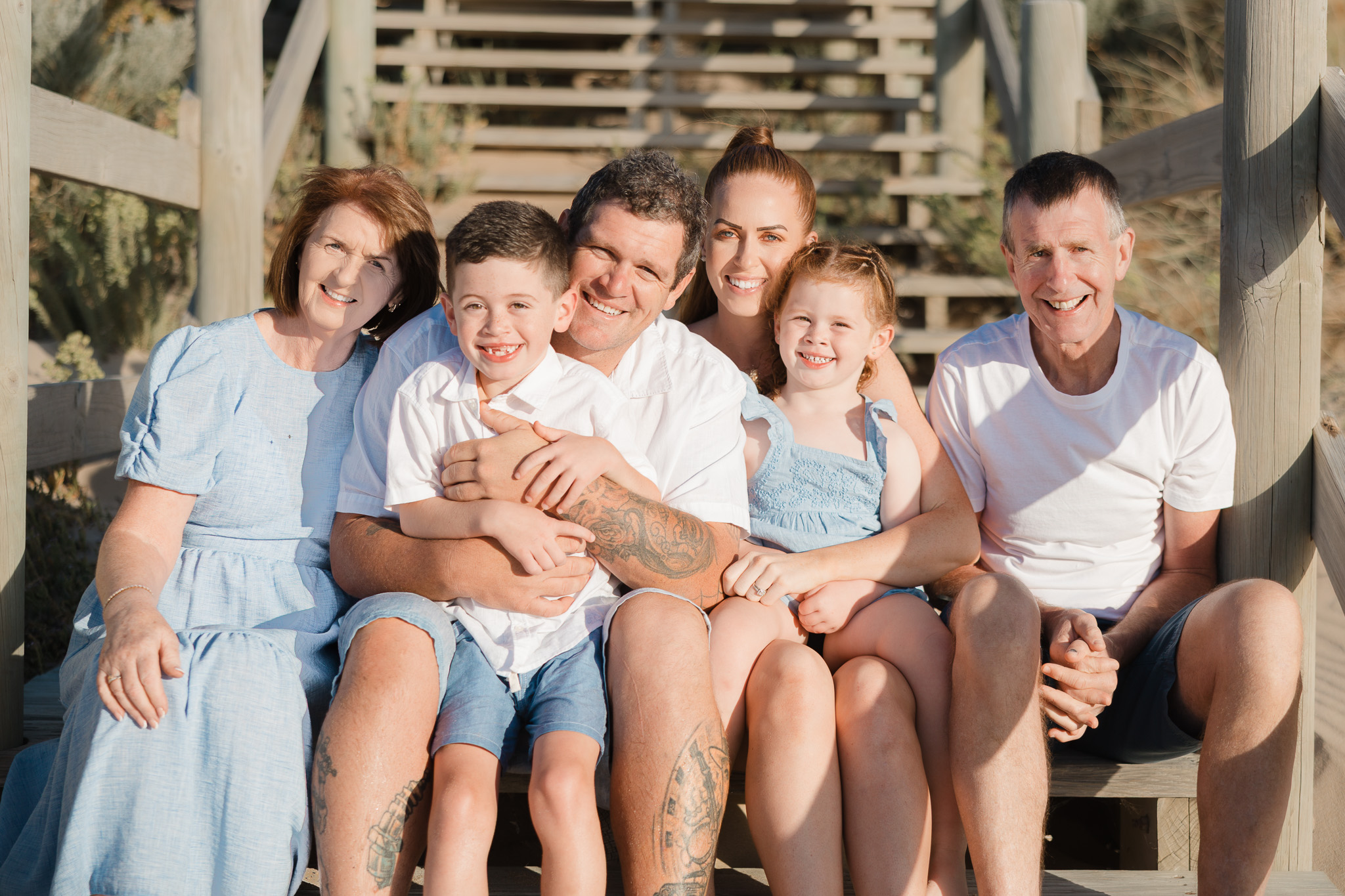 Three generations of a family smiling together on wooden beach stairs near the coast