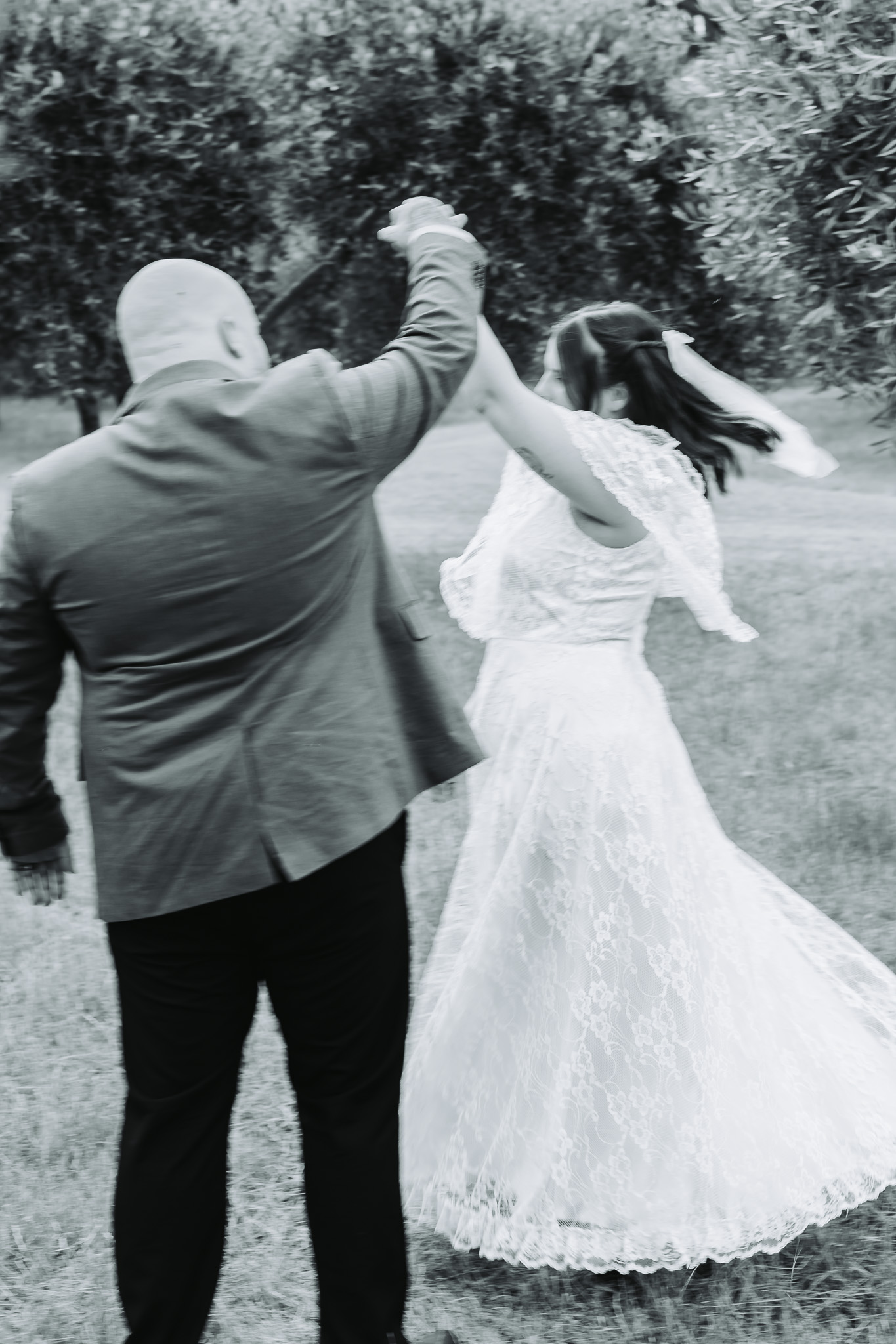 Black and white photo of a bride and groom spinning while dancing outdoors