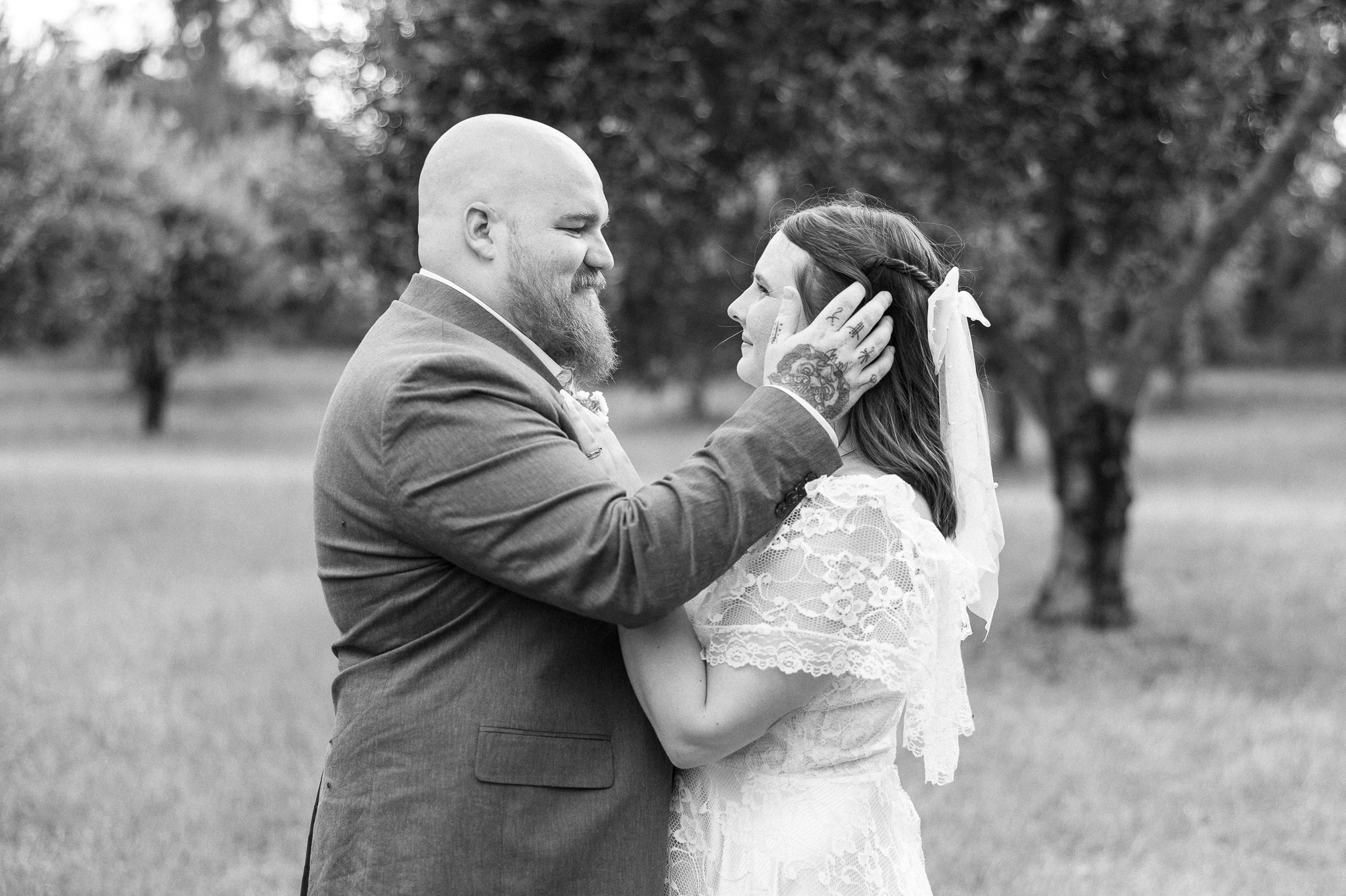 Black and white portrait of a bride and groom touching foreheads in a grassy outdoor setting