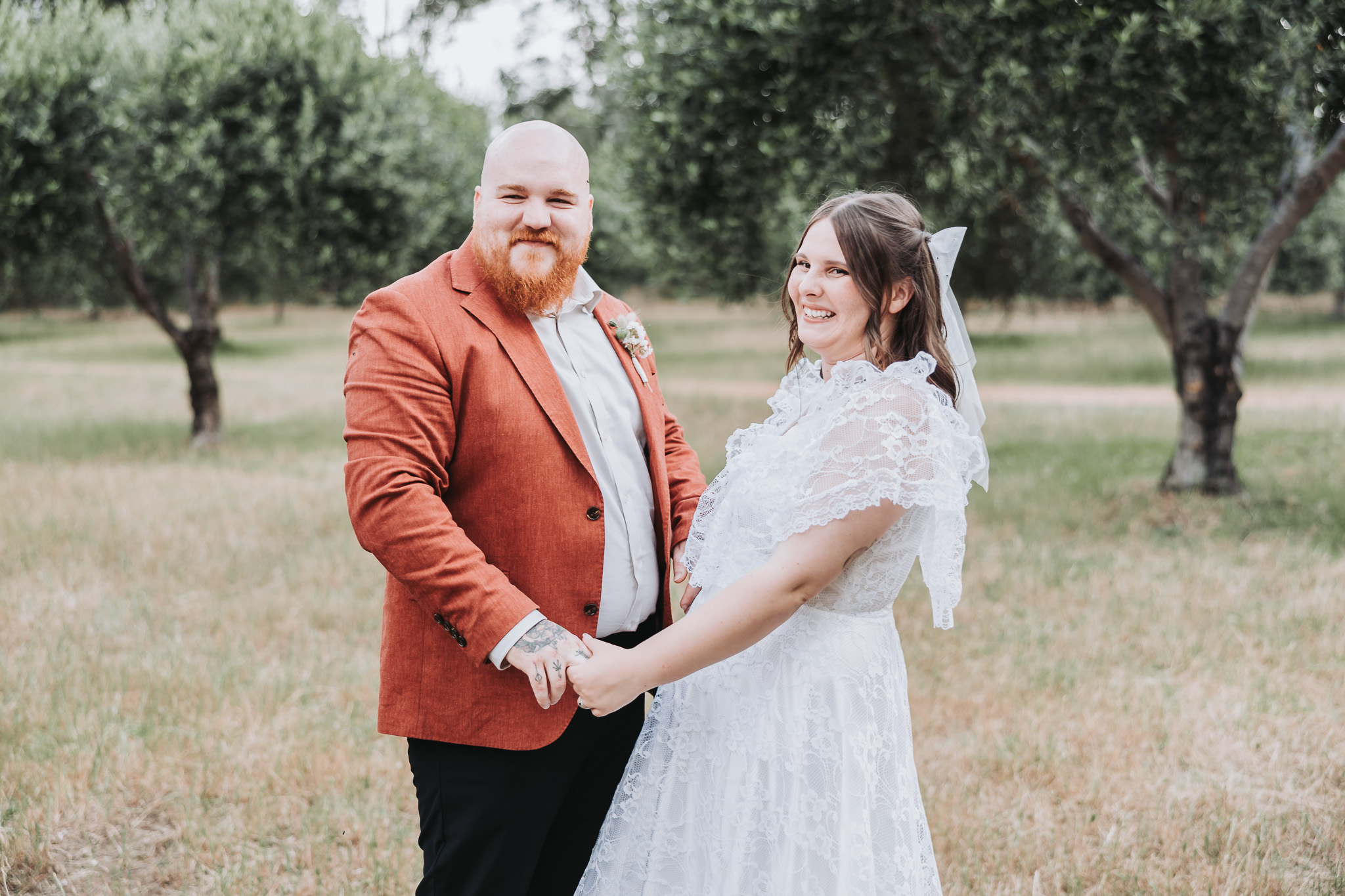 Smiling newlywed couple holding hands in dry grass among olive trees at a Perth wedding