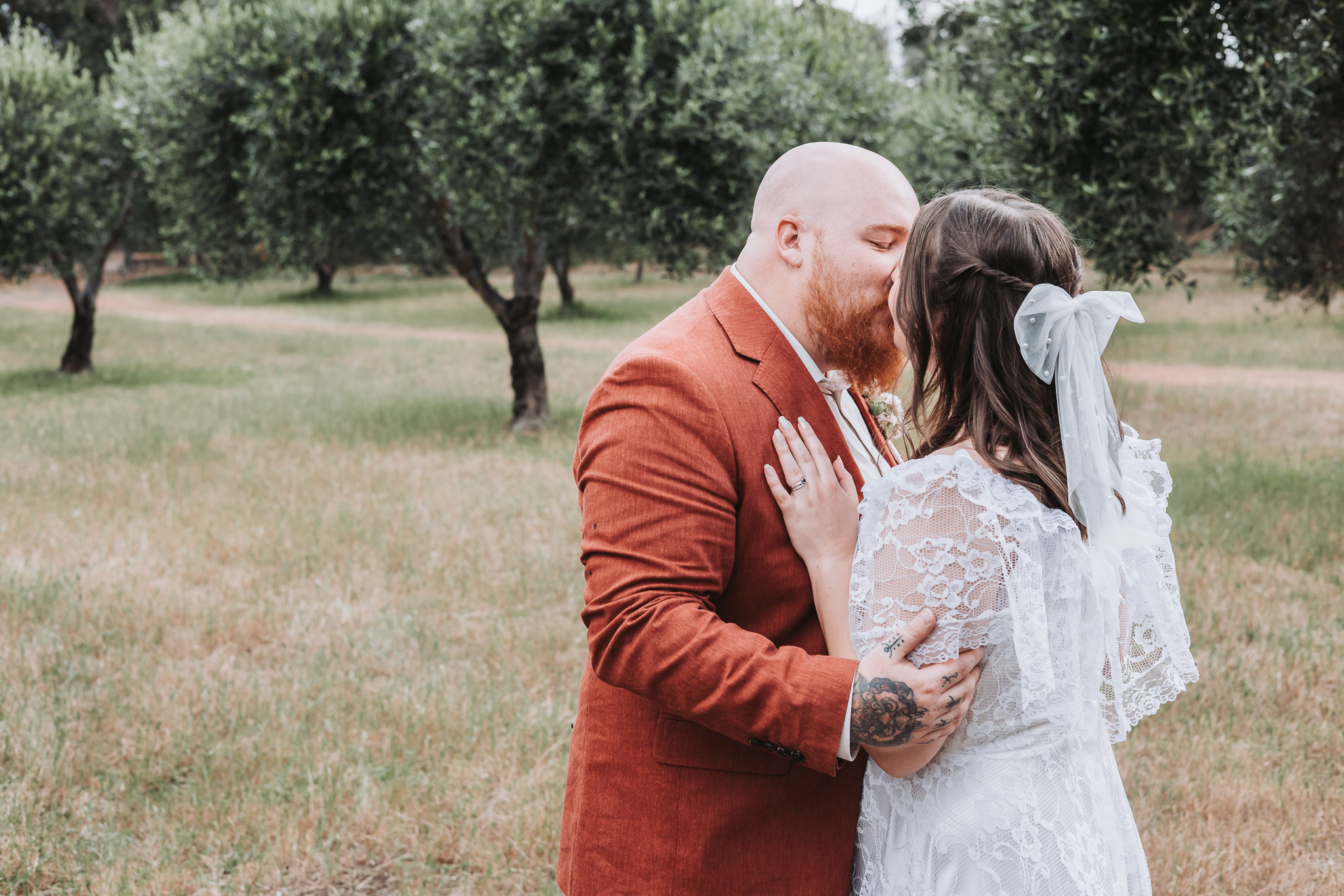 Bride with a pearl tulle bow and groom in terracotta kissing in an olive grove