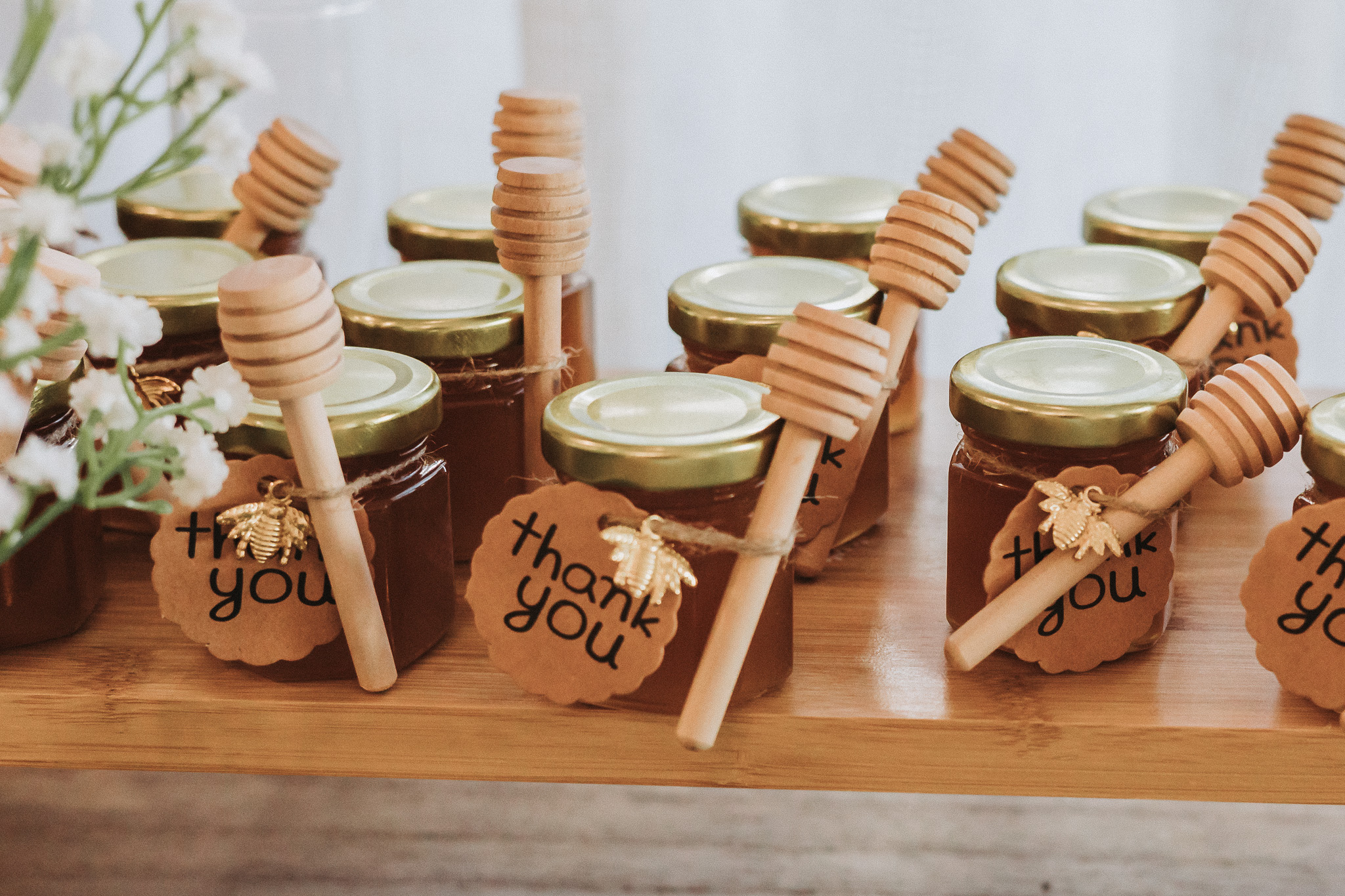 Rows of honey jar wedding favours with wooden dippers and thank-you tags on a wooden table